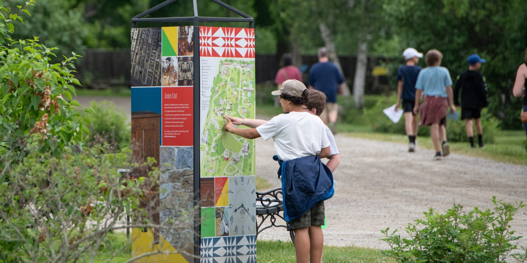 Young visitor pointing at a trail map while others walk ahead on a summer day in Shelburne