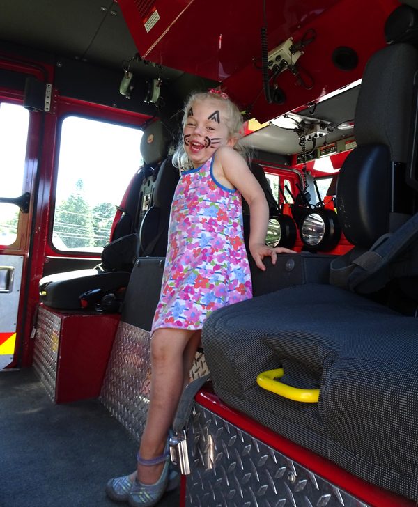 Girl with cat face paint grinning inside a fire truck