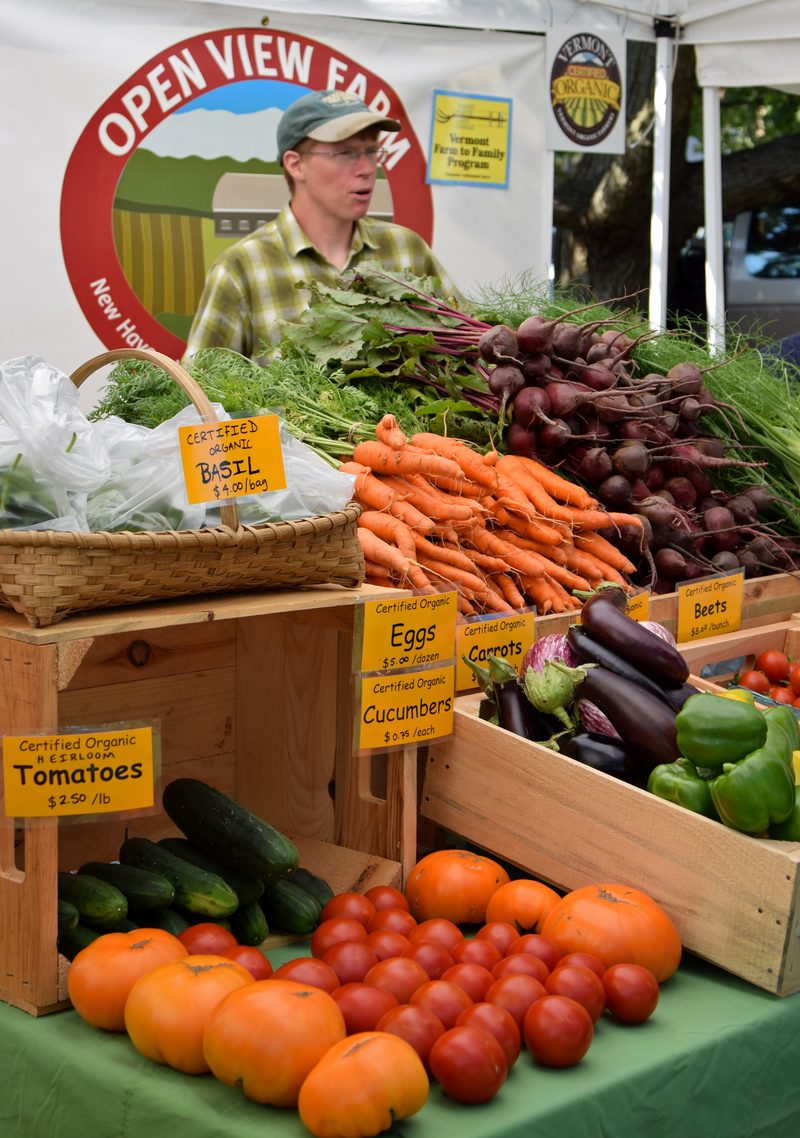 Open View Farm vendor behind a full produce stand at the market