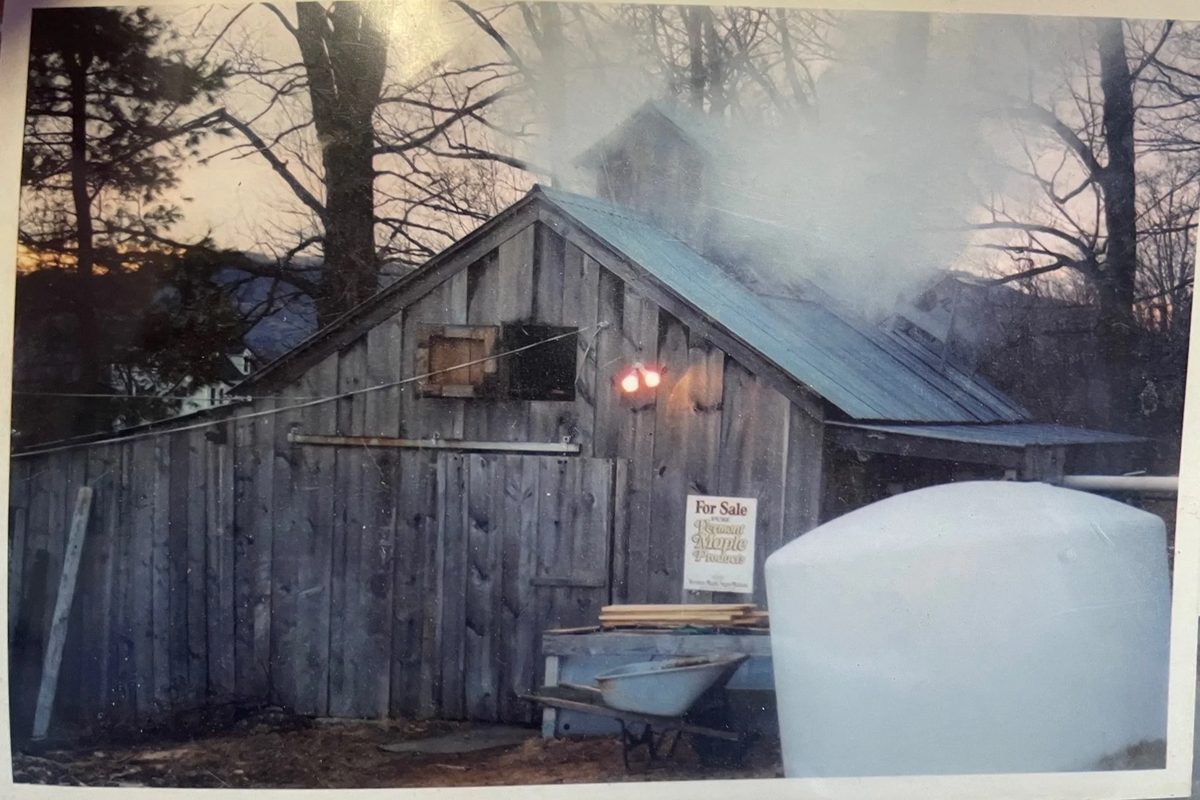 The sugarhouse at dusk with steam rising from the roof during a boil, a Pure Vermont Maple Products sign on the wall.