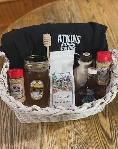 A basket holding a jar of honey, maple syrup, pancake mix, seasoning shakers and a farm T-shirt.