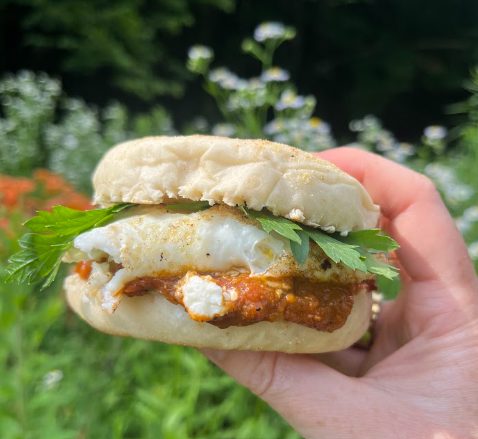 A shakshuka sandwich — stewed tomato and pepper, feta, egg and parsley on an English muffin.