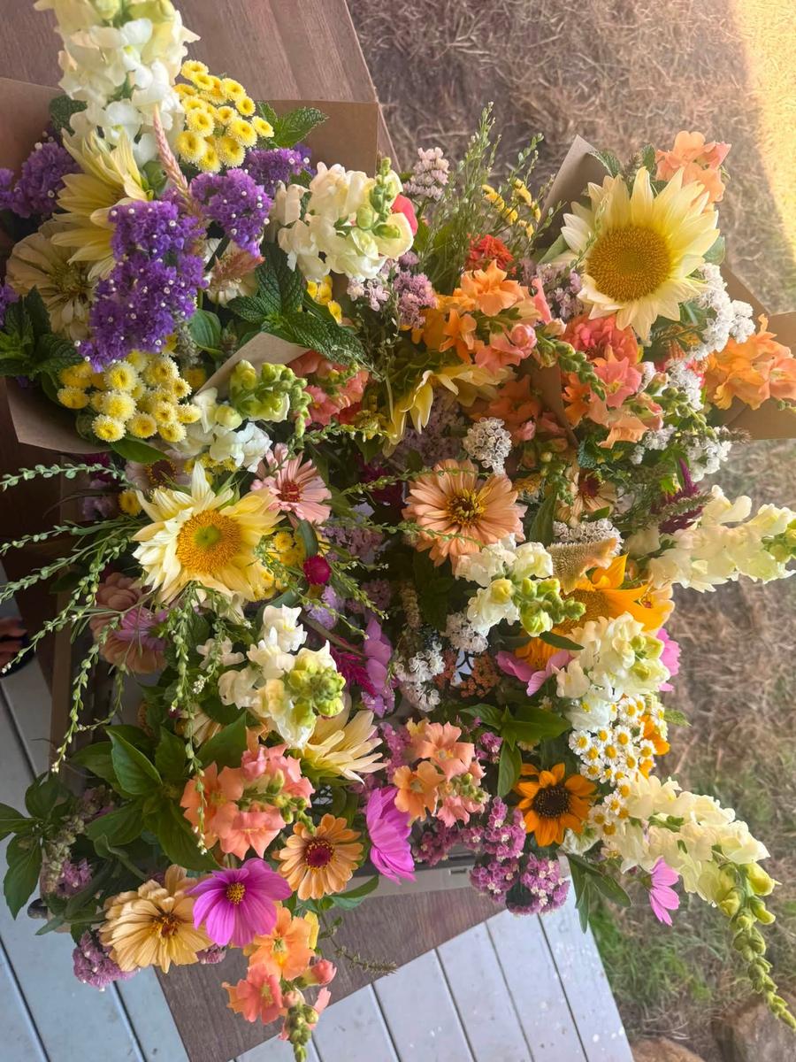 An overhead view of a bouquet of snapdragons, sunflowers, and statice in yellow, purple, and orange.