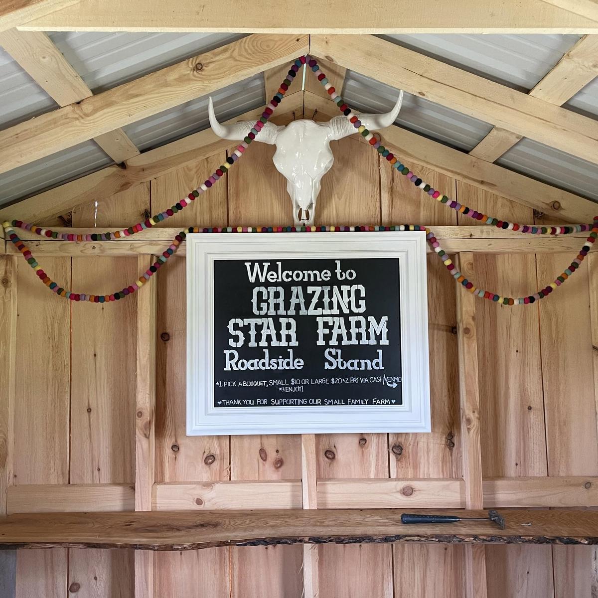 Inside the roadside stand: a chalkboard welcome sign under a longhorn skull and a garland, thanking customers for supporting a small family farm.