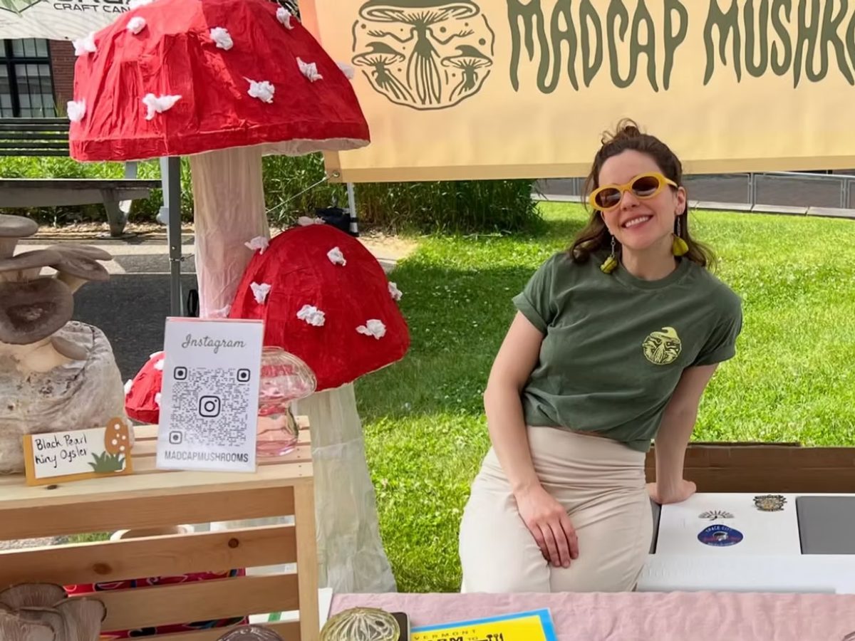 Lindsey Goldberg at the Madcap Mushrooms market booth, beside painted toadstool decorations and the farm banner.
